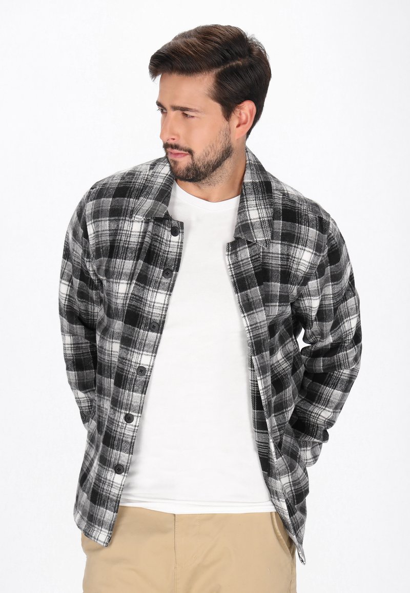 Musta-valkoinen ruudullinen flanellipaita, jossa on pitkät hihat, napit edessä ja hieman oversize-istuvuus, sen päällä valkoinen t-paita.