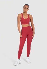 Rood sportbeha- en bijpassende legging-set van een gladde, rekbare stof. Witte sneakers met veters. Eenvoudig ontwerp, zonder zichtbare patronen of accenten.