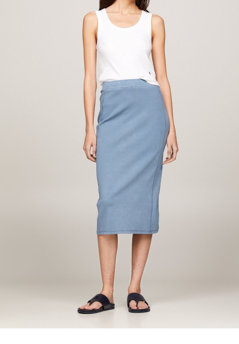 Jupe midi bleu clair en tissu doux avec une taille ajustée et une coupe droite. Portée avec un débardeur blanc et des sandales slides noires.
