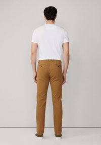 Chinos de algodón marrones con un ajuste aerodinámico y bolsillos traseros con botón, combinados con una camiseta blanca básica y zapatillas informales.
