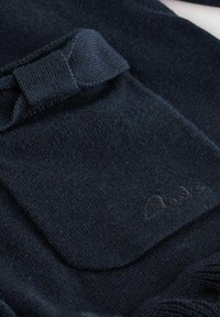 Marinblått stickat tyg med en mjuk textur, som har en ficka och en rosettdetalj. Inkluderar subtil broderad märkning i hörnet.