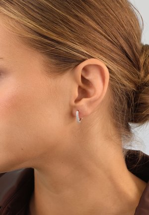 Silver hoop earring with a curved shape, featuring small embedded crystals along the surface, worn on a light skin tone.