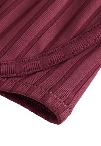 Primo piano di tessuto a coste piegato in bordeaux intenso con dettagli di cuciture visibili e motivo a maglia testurizzato.