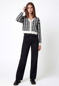Zwart-witte houndstooth cropped cardigan met een V-hals en knoopsluiting, gecombineerd met hooggetailleerde zwarte broek en zwarte schoenen.