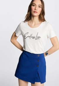 T-shirt bianco con la scritta "Endless Love", abbinato a una mini gonna blu con frontale a pattina e dettagli in bottone dorato.