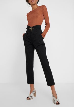 Rust ribbed long-sleeve top, high-waisted black trousers with belted detail, and patterned open-toe heeled shoes with a wooden block heel.