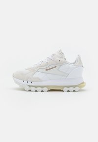 Vit Reebok-sneaker med beige mockadetaljer, strukturerad gummisula, quiltade sidopaneler och varumärkeslogotyp på sidan och tungan.
