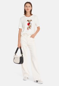 Witte t-shirt met hondenafbeelding, gecombineerd met hoge witte jeans en een bicolor handtas in zwart en Roomwit. Gladde stof, losse pasvorm.