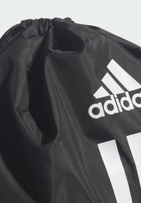 Bolsa negra con cordón hecha de un material de nailon texturizado, que presenta un prominente logo blanco de Adidas y tres rayas blancas.