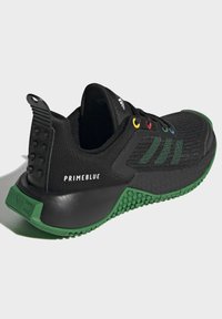 Černé tenisky Adidas Primeblue s zelenou podrážkou, texturovaným gripem, vícbarevnými očky a černým síťovaným svrškem, který zdobí zelené pruhy Adidas.