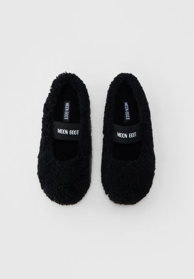 Paire de chaussons noirs en peluche avec des sangles élastiques portant l'inscription "MOON BOOT", sur un fond blanc uni.