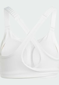 Balta sporta krūšturis ar krusteniskām siksnām, gludu tekstūru, atslēgas caurumu aizmugurē un elastīgu jostu atbalstam.