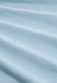 Tela de color azul claro con una textura suave, que presenta sutiles variaciones en el tono, plegada para crear suaves ondas y curvas.