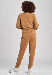 Brun bomullscrewneck sweatshirt med matchande avsmalnande joggers. Har ribbad muddar och midjeband, ihop med vita och beige sneakers.