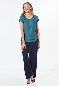 Türkises kurzärmliges Oberteil mit gepunktetem Design, kombiniert mit marineblauen weit geschnittenen Hosen und schwarzen Sandalen. Glatter Stoff und lockere Passform.