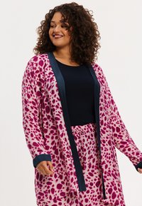Langes, pink und cremefarbenes Kimono mit Leopardenmuster, ausgestattet mit dunkelblauen Ärmeln und Besatz, getragen über einem schwarzen Top. Weicher, fließender Stoff.