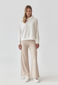 Outfit casual composto da una felpa bianca con cappuccio e pantaloni a gamba larga beige realizzati in un tessuto morbido e testurizzato, abbinati a sneaker bianche.