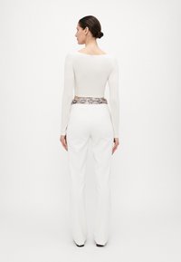 Top cropped bianco con maniche lunghe abbinato a pantaloni bianchi a vita alta con cintura in stampa pitonata. Texture liscia, stile aderente.
