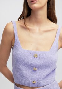 Lila crop top met een textuurstof, vierkante halslijn en drie gouden knopen aan de voorkant. Dunne bandjes complementeren het ontwerp.