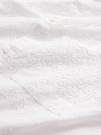 Hvit bomullsstoff med broderte blomsterdesign. Har knapper og delikat, teksturert detaljering i stoffdesignet.
