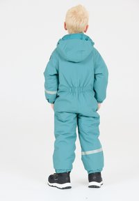 Teal vattentät snälldräkt med huva, elastisk midja och reflekterande detaljer; matchad med svarta vattentäta stövlar och strukturerade sulor.