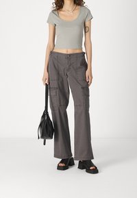 Šedé zkrácené tričko, volné šedé cargo kalhoty s kapsami, černé platformové sandály a malá černá kabelka. Minimalistický design a ležérní střih.