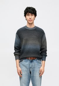 Temno sivi pulover z degradiranim učinkom, z rebrastim izrezom in manšetami, nošen čez svetlo modre jeans hlače. Tkanina je videti strukturirana in mehka.