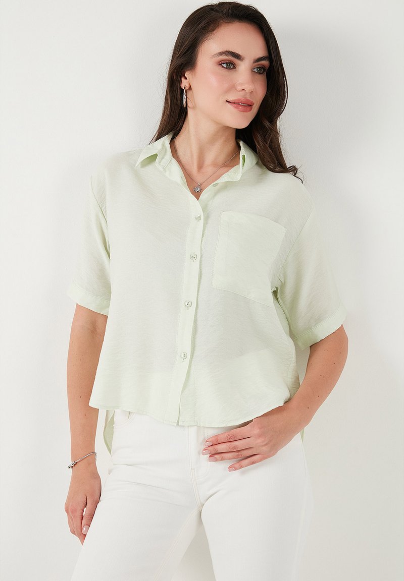 Camicia button-up verde chiaro a maniche corte con una tasca sul petto. Realizzata in un tessuto testurizzato con una vestibilità leggermente ampia e un orlo arrotondato.
