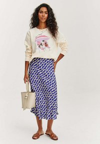 Mikina ve světle krémové barvě s grafikou psů na plážových křeslech. Plynoucí modrá sukně s bílým cik-cak vzorem. Hnědé sandály.
