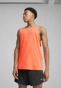 Lys orange tanktop lavet af letvægtsstof, med et lilla logo, sideløsning og parret med sorte shorts.