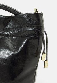 Mustapokkinen nahkabucket-laukku kiiltäväpintaisella pinnalla, naruella suljettava ja kultaisilla metalliosilla. Pyöreä muoto ja teksturoitu pinta.