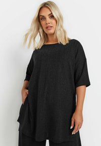 Top nero largo con maniche corte, caratterizzato da un motivo rigato testurizzato e un ampio scollo. Include tasche laterali per maggiore funzionalità.