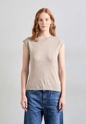 Beige sleeveless top made of textured fabric with a round neck, paired with dark blue loose-fit denim jeans.