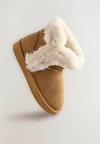 Braune Wildleder-Stiefeletten mit einem flauschigen weißen felltrim, die eine abgerundete Zehenpartie und eine strukturierte Sohle aufweisen, vor einem neutralen Hintergrund schwebend.