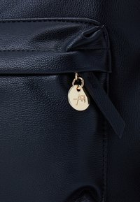 Navy textured leather bag featuring a front pocket, gold hardware, and a small logo tag. Smooth finish with a sleek design.