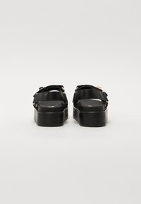 Black platform sandals with wide straps, silver buckles, and a smooth leather texture. Flat sole with a slight heel and no visible patterns.