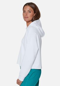 Witte cropped hoodie met capuchon, met een ontspannen pasvorm en geribde manchetten, gecombineerd met teal broek, met een gladde stoftextuur.