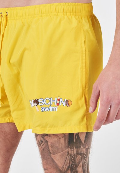 Shorts da bagno gialli realizzati in tessuto leggero, con cintura elasticizzata e un giocoso logo "Moschino swim" con accenti colorati.