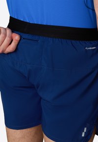 Blue shorts with a black waistband, featuring a small zippered pocket and a "FLASHDRY" label on the side. Smooth texture and fitted design.