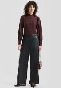Bordowa teksturowana bluzka z długim rękawem z bufkami na ramionach, zestawiona z czarnymi, szerokimi spodniami ze skóry o wysokim stanie oraz małą torebką z metalicznymi akcentami.