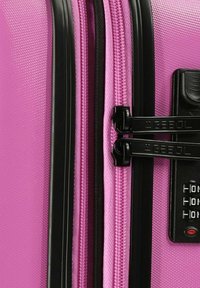 Valigia rigida rosa con superficie testurizzata, hardware della cerniera nera e lucchetto a combinazione. Presenta doppie cerniere e un design elegante.