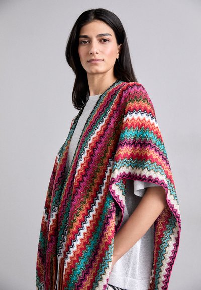 Poncho multicolor con un patrón en zigzag en vibrantes tonos de rosa, turquesa y dorado, hecho de una tela texturizada con bordes desflecados.