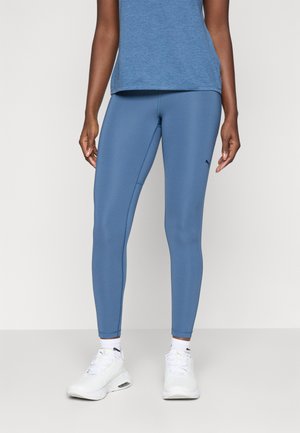 Leggings atletice albastre dintr-un material elastic, cu o textură netedă și un design ajustat, asociate cu un top albastru și adidași albi.