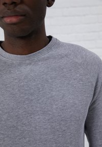 Sweatshirt gris avec un col rond côtelé, tissu texturé et manches raglan. Présente des détails de couture subtils le long des coutures.