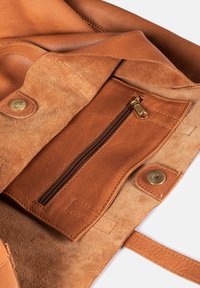 Tasche aus hellbraunem Leder mit einem Innenfutter aus Wildleder, einem Reißverschlussfach und Druckknopfverschlüssen. Glatte und strukturierte Materialien mit goldenen Beschlägen.