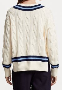 Creme kabelstickad tröja med ribbad nederkant och ärmslut. Har en marinblå och ljusblå randig krage. Bakifrån visas den texturerade mönstret.