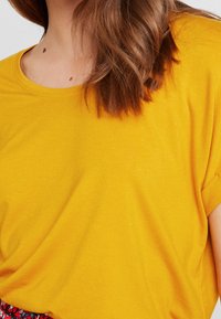 T-shirt giallo a maniche corte con scollatura rotonda e tessuto morbido. La vista ravvicinata mette in risalto il colore vivace e la superficie liscia.