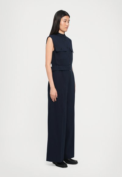 Navy sleeveless jumpsuit with a collar, two chest pockets, and a belted waist, featuring wide-leg pants and smooth fabric texture.