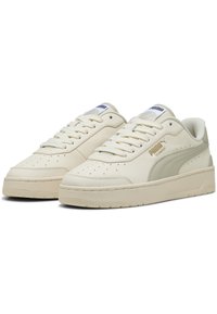 Adidași de culoare crem, cu o parte superioară din piele netedă, vârful perforat și accente gri subtile. Au șireturi albe și o talpă din cauciuc texturat.