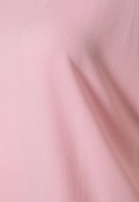 Světle růžová látka s hladkým, mírně lesklým povrchem; má měkký, elastický pocit, vhodná pro pohodlné nošení.